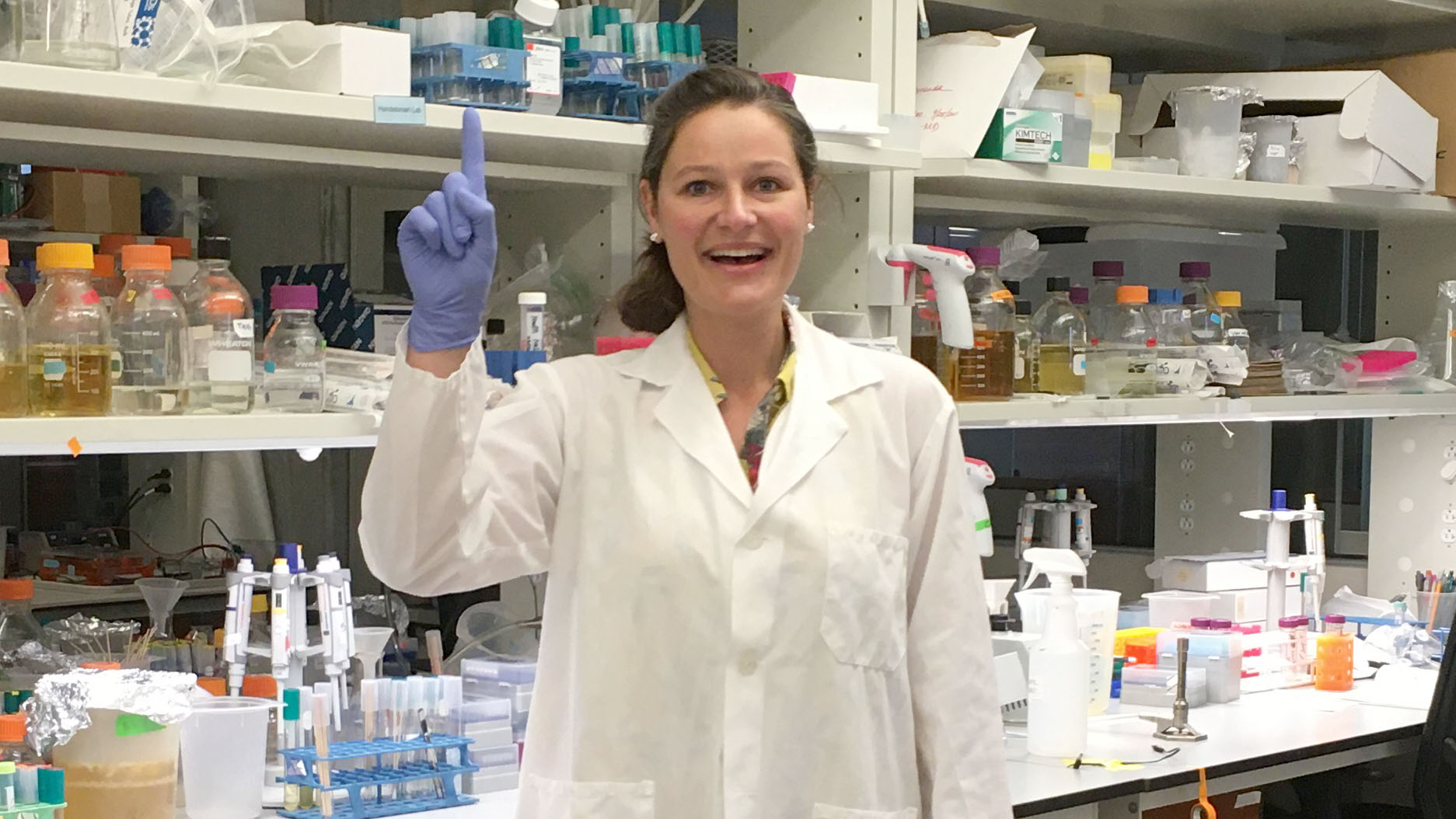 Scientist in white lab coat pointing up at tabs