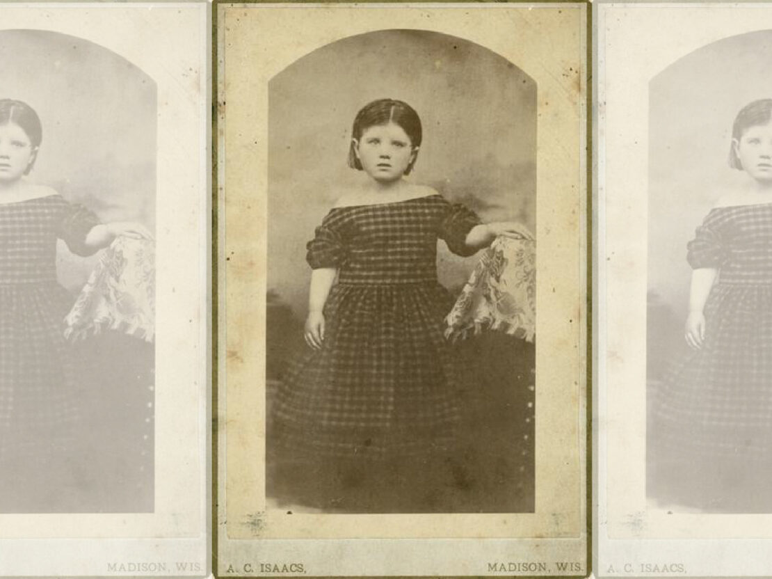A framed black and white photograph of Belle as a young girl. She wears a long dress and rests her left hand on a covered stand. She looks to the right of the viewer, with a serious expression on her face.