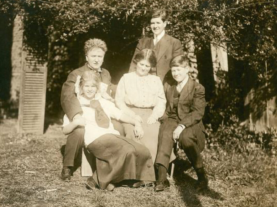 A black a white photograph of the Bob, Belle, and their children seated outside with trees behind them.