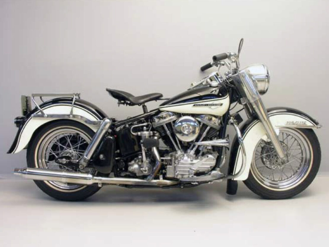 A color photograph of a white, silver and black motorcycle in front of a plain off-white background.