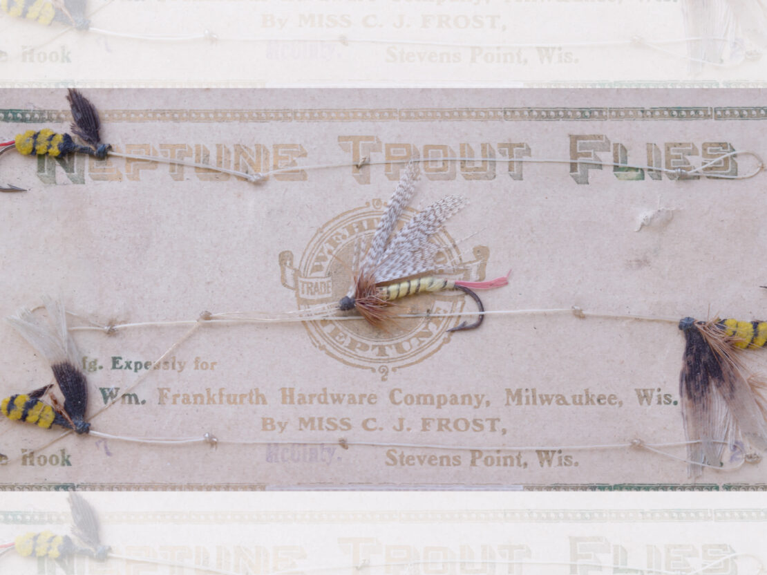 A piece of paper with the heading, “Neptune Trout Flies” above and “By Ms. C.J. Frost Stevens Point, Wis” at the bottom, with a series of flies attached.