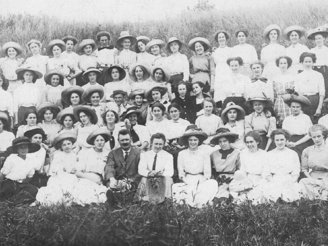 A black and white photograph of a large group of mostly women seated in a grassy area outside, posing for a picture.