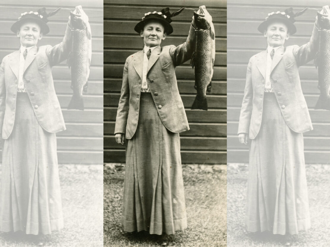 A black and white photo of Carrie standing in front of a building, proudly holding up a large fish.