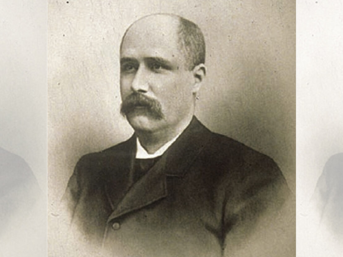 A black and white photograph of a middle-aged Charles Clark. In the photo, Clark is looking to the left of the viewer, with his mouth closed and arms by his sides.