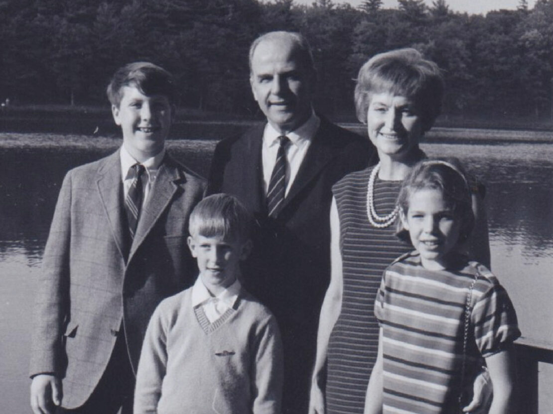 A black and white photo of Gaylord with his wife and three children, posing for a photo outside in front of water and trees.