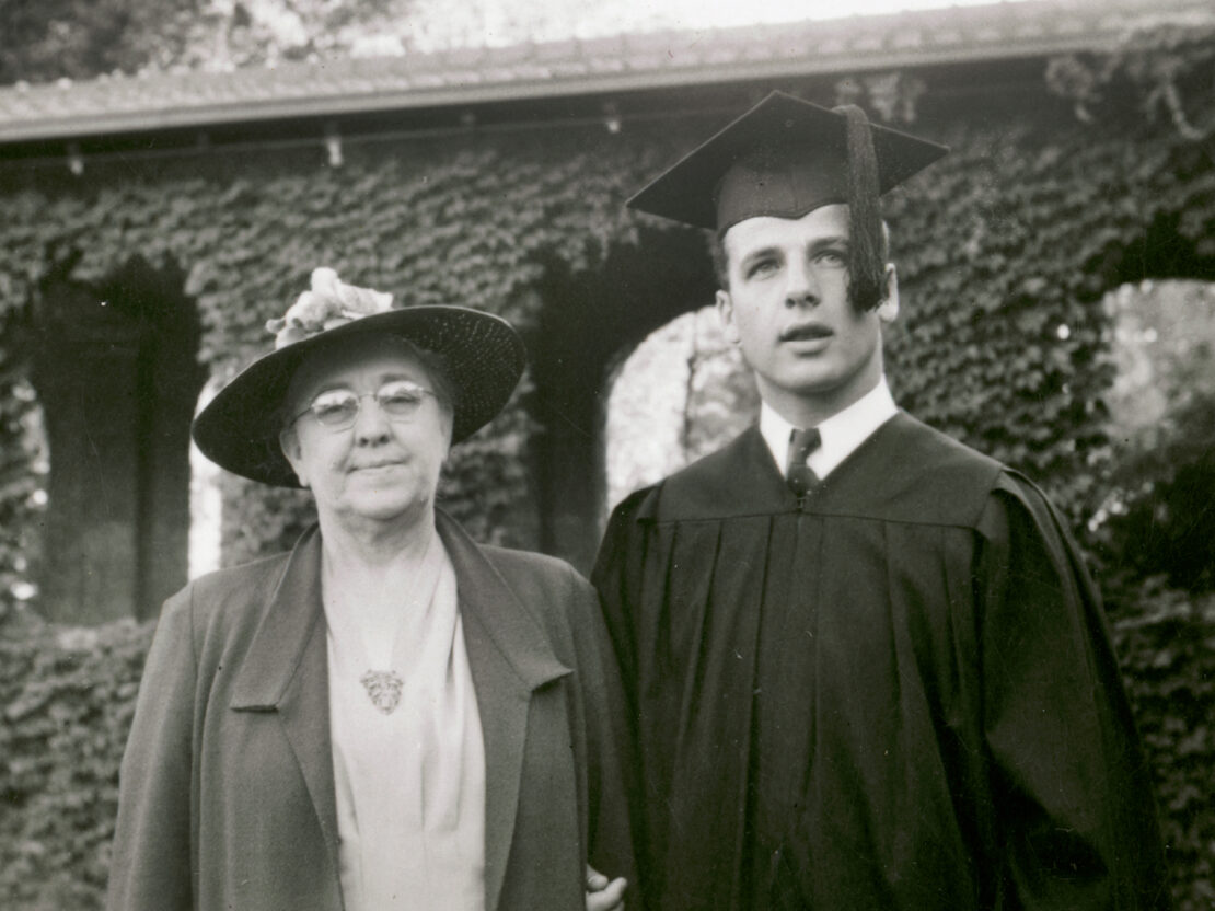 In this black and white photo, Gaylord stands next to his mother. He is wearing a graduation cap and gown and has his right hand around his mother's arm.