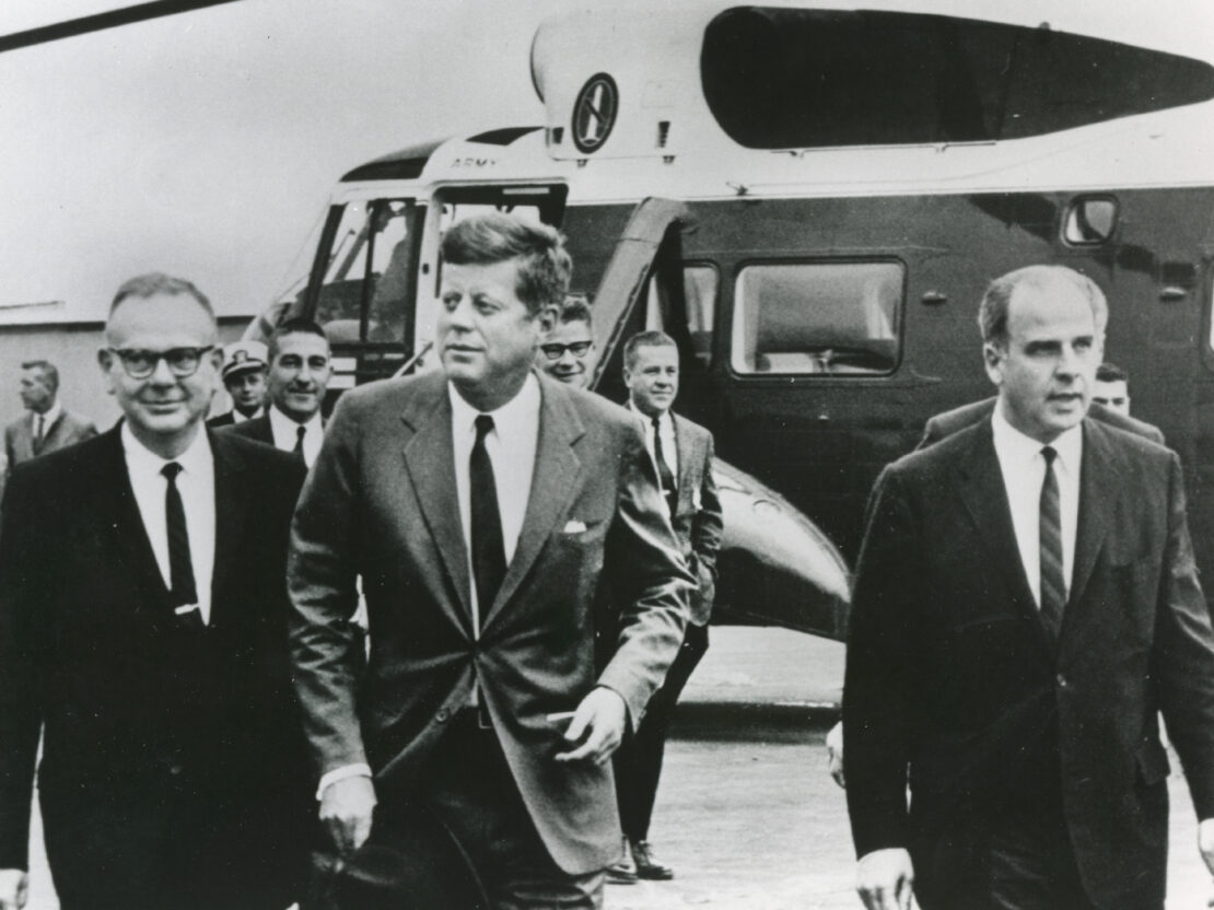 A black and white image of President John F. Kennedy and Gaylord Nelson walking away from a helicopter.