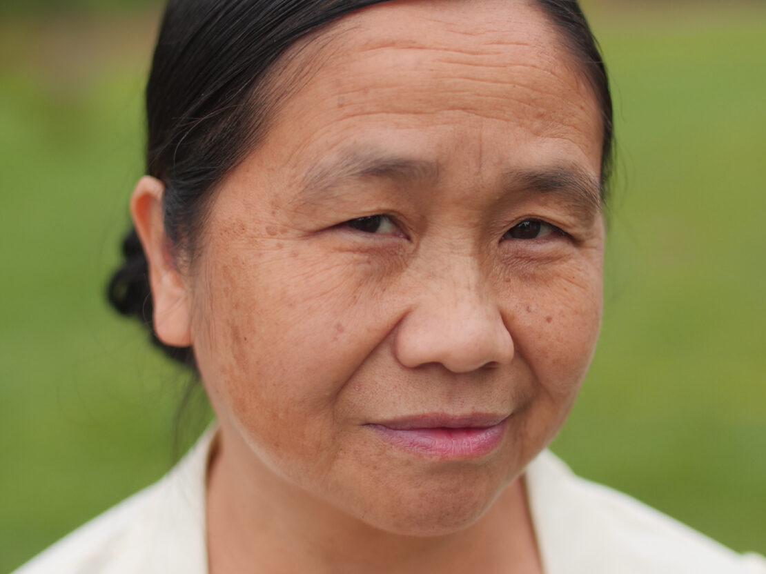 A color portrait of Ta Moua. Her head and shoulders are visible and the background behind her is a vibrant green color.