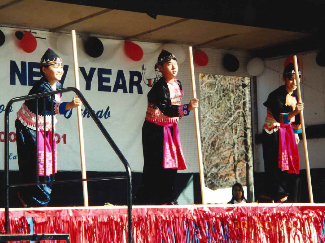 A color image showing three people on stage in front of a sign that includes the words “New Year.”