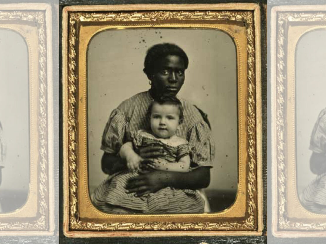 An image of a Black woman seated, holding a white baby, looking at the viewer. The image is in a gold frame.
