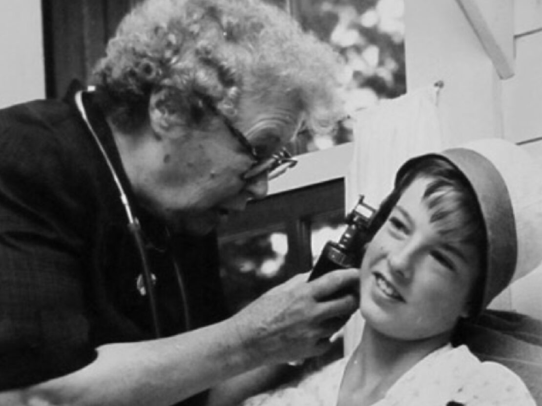 A black and white image of Doctor Kate holding up a scope to look inside a boy's ear.