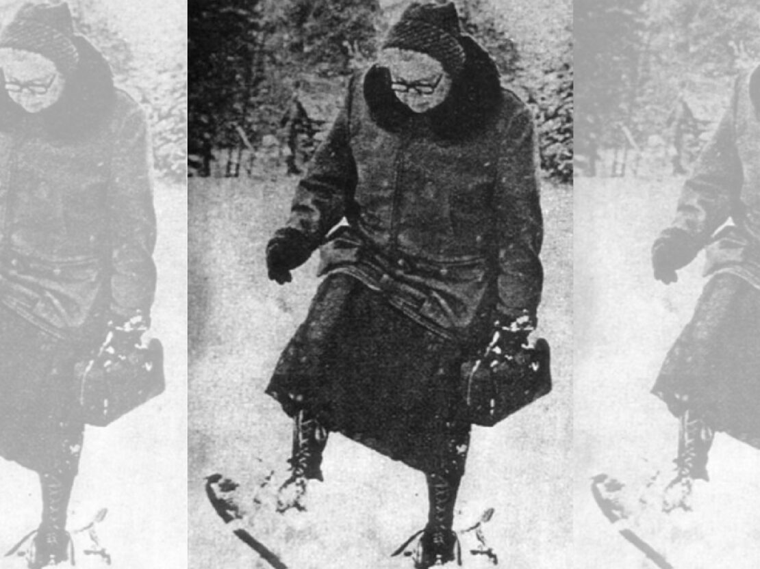 A black and white photograph of Dr. Kate outside in winter, walking through the snow while wearing snowshoes.