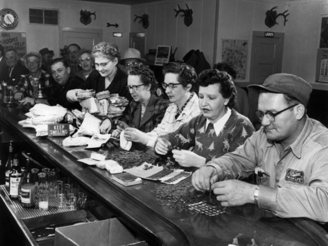 A black and white image of four people seated, counting pennies.