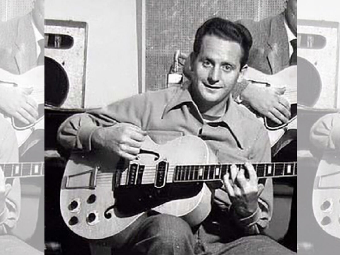 A black and white photograph showing Les Paul seated, and holding a guitar, and looking at the viewer.