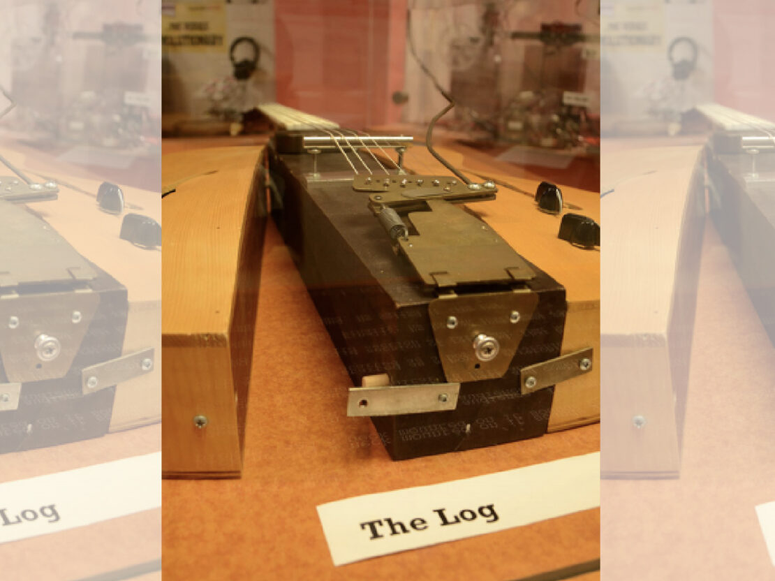 A color photograph of rectangular instrument with metal fixtures and strings connected to a piece of wood. Below the instrument is a white piece of paper with the words “The Log” on it.