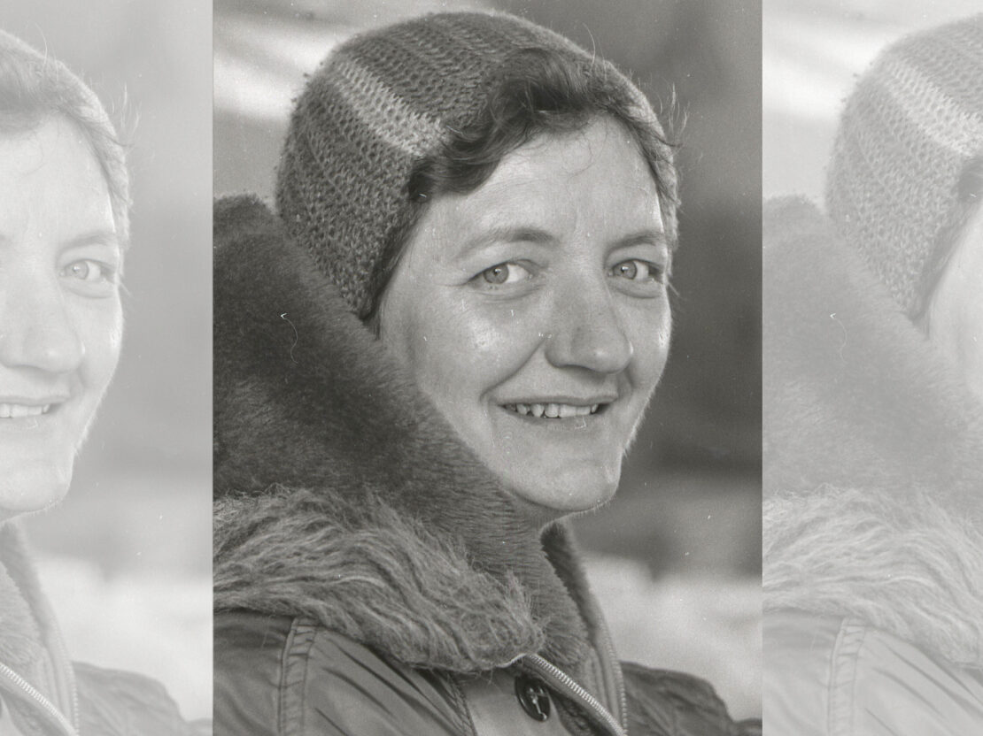 A black and white portrait of Jenny Ehl. She is wearing a coat and hat and is smiling at the viewer.