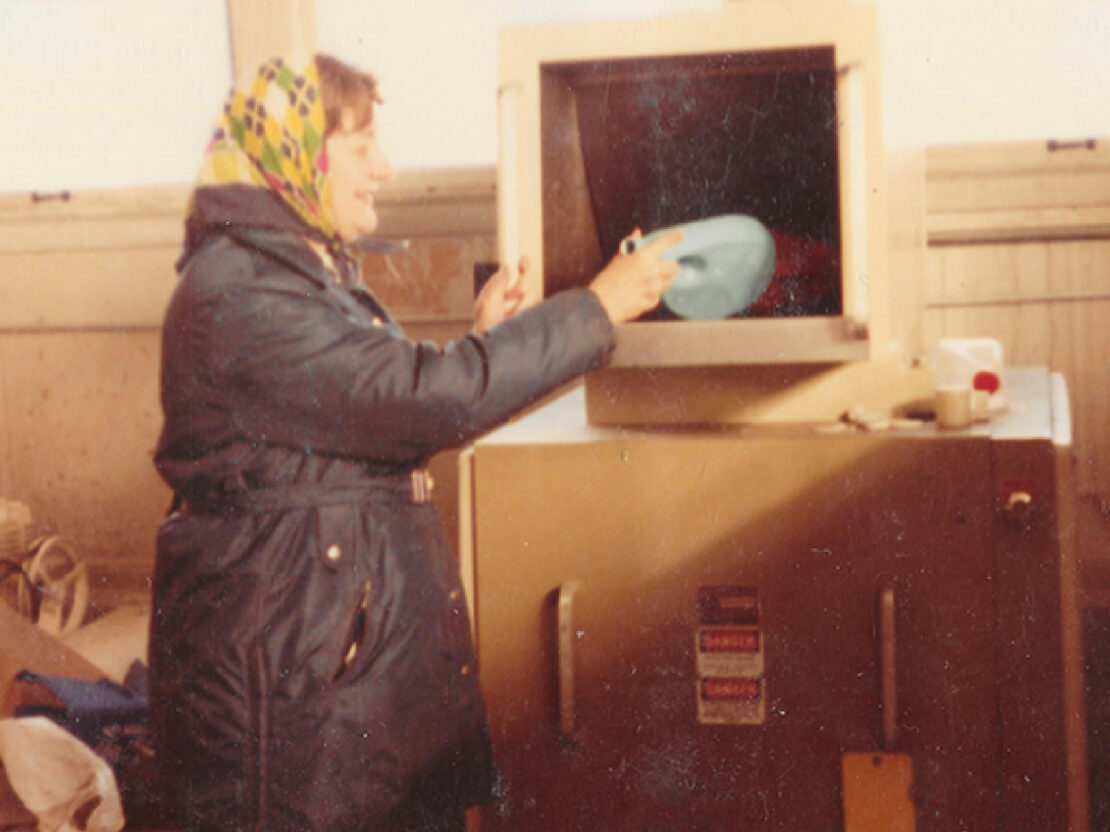 A color photograph showing Jenny Ehl holding an item in front of the chute of the plastic grinder.