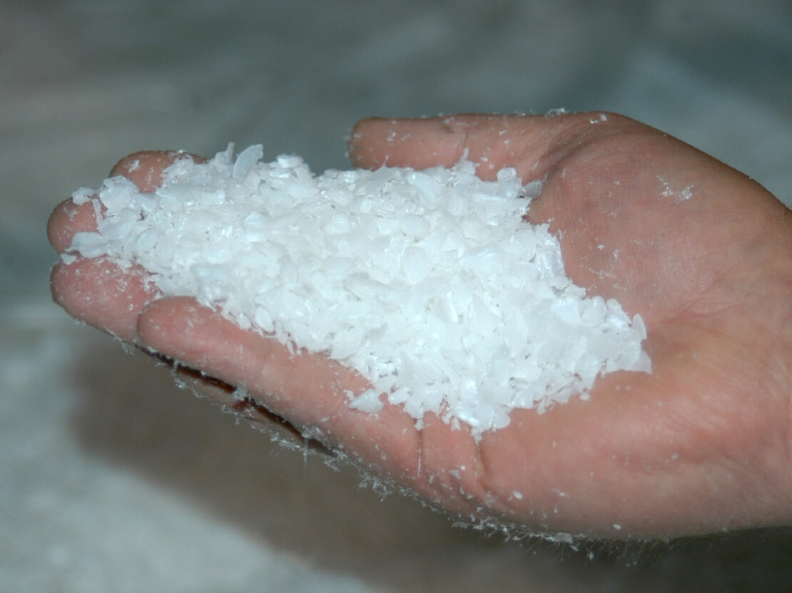A color photograph showing a hand, turned towards the viewer, holding small, white pieces of ground-up plastic.