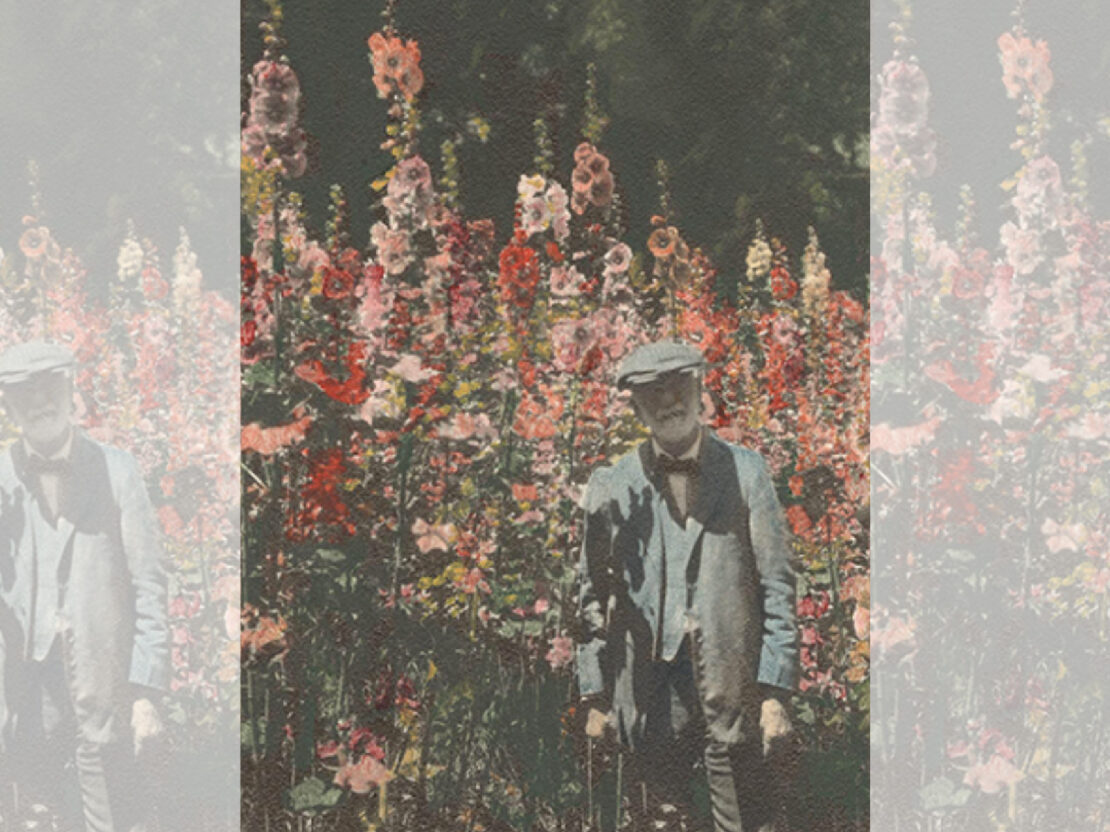 A color image of Stephen standing outside in front of a wall of brightly colored flowers.