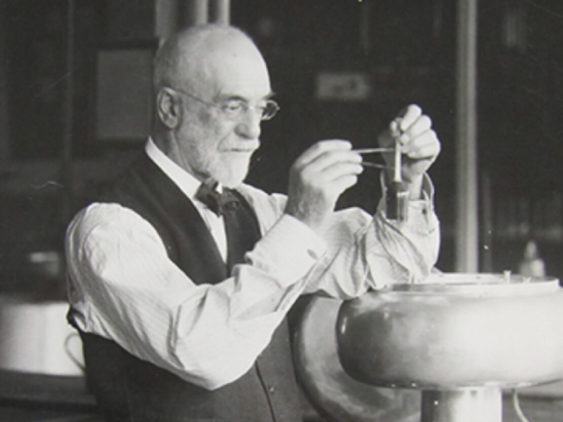 A black and white image of Stephen holding up parts of an instrument and looking closely at them.
