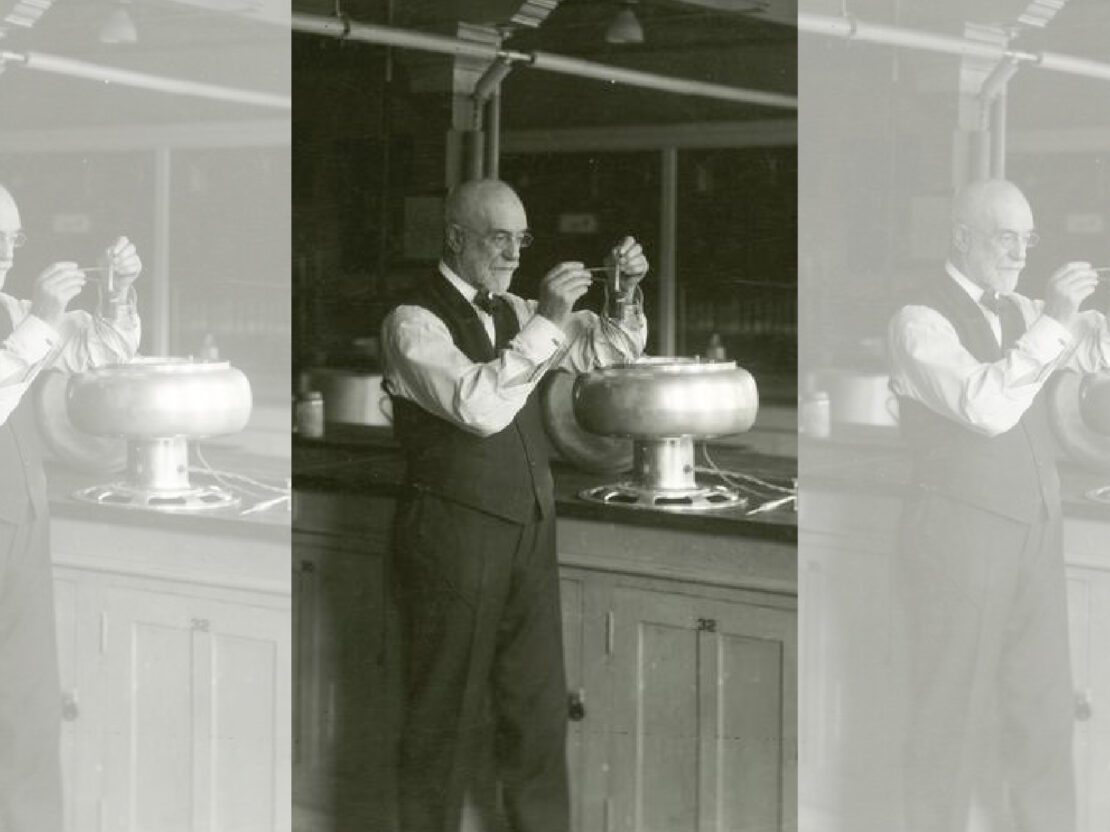 A black and white image of Stephen holding up parts of an instrument and looking closely at them.