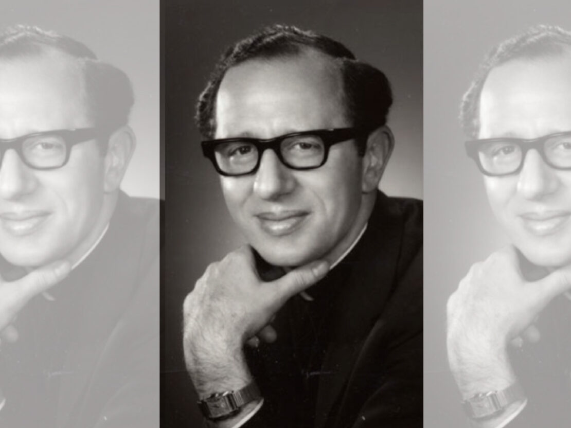 A black and white portrait of Father James Groppi. He holds his chin in his hand and looks at the viewer.