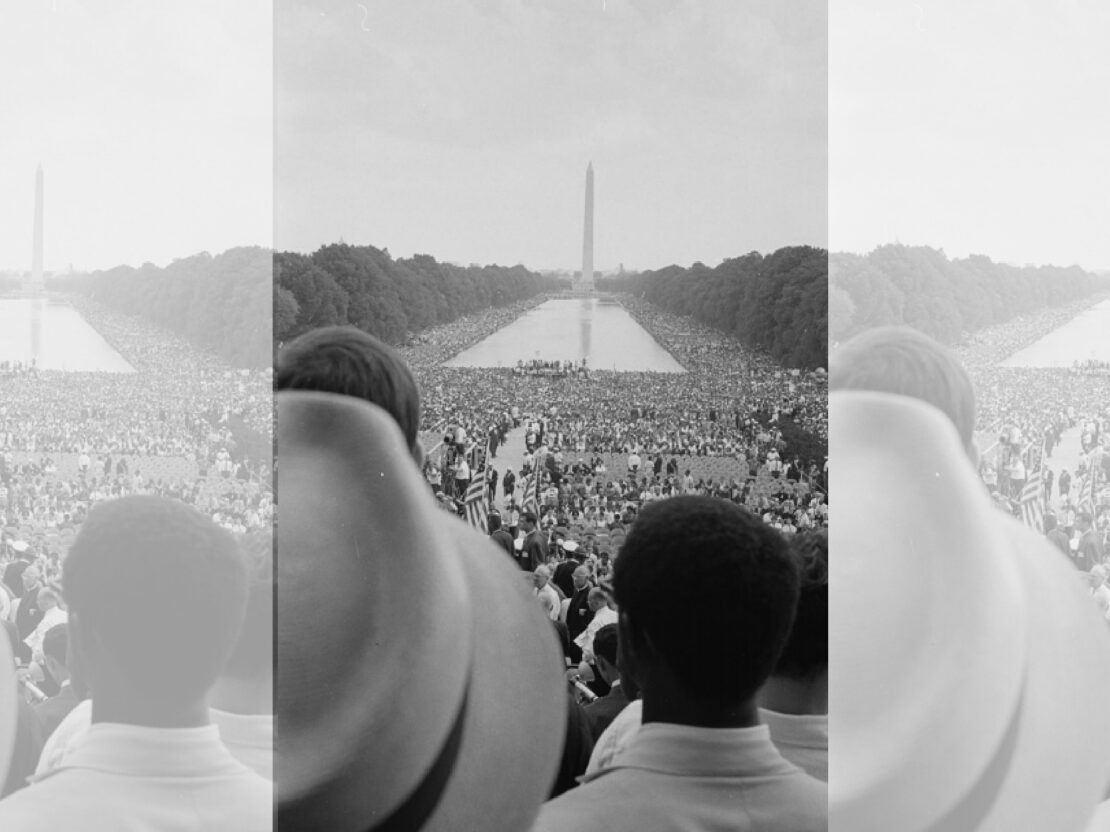 A black and white photograph taken from in the crowd looking out over a sea of people, with the Washington Monument straight ahead in the distance.