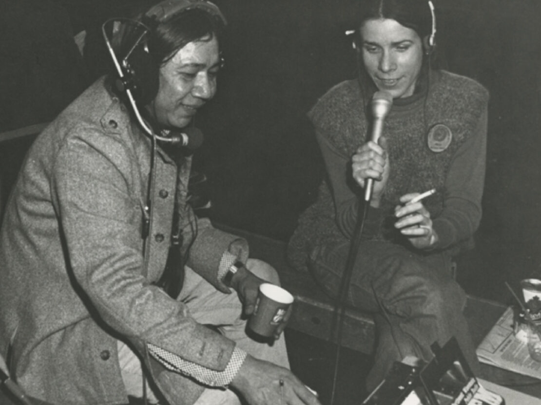 A black and white photograph of Walter seated next to another person. Both are wearing headsets and the other person is speaking into a handheld microphone.