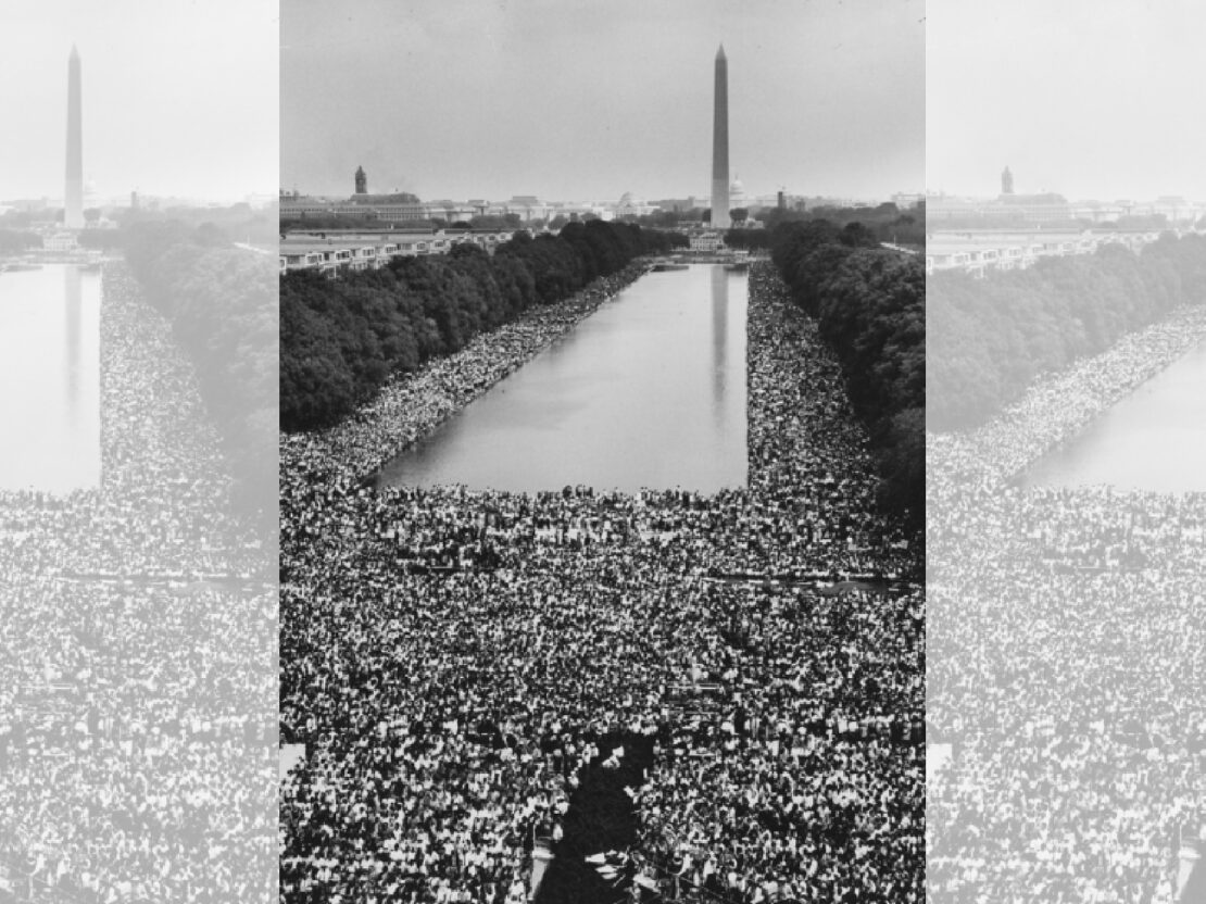 A black and white photograph of the national mall filled with people. The Washington Monument is visible in distance.