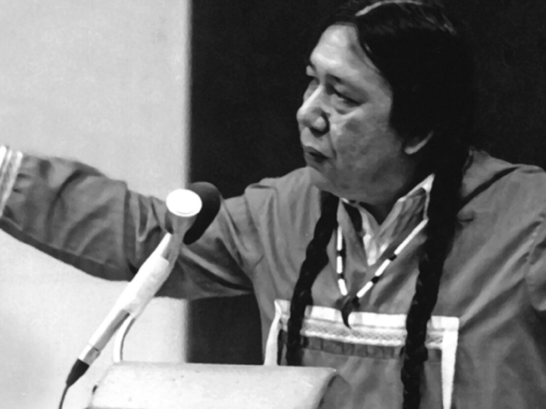 A black and white photograph of Walter standing behind a microphone with his arms outstretched.
