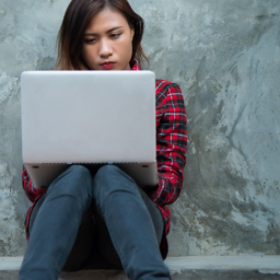 Person sitting with back up against wall and laptop on their lap