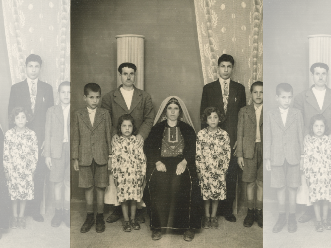 A black and white photograph showing Mahmoud Othman Atta as a boy. He is wearing a dark suit and is standing with his two brothers and two sisters. His mother sits in the center of the photo wearing a dark dress. His uncle is in a grey suit standing to the left.