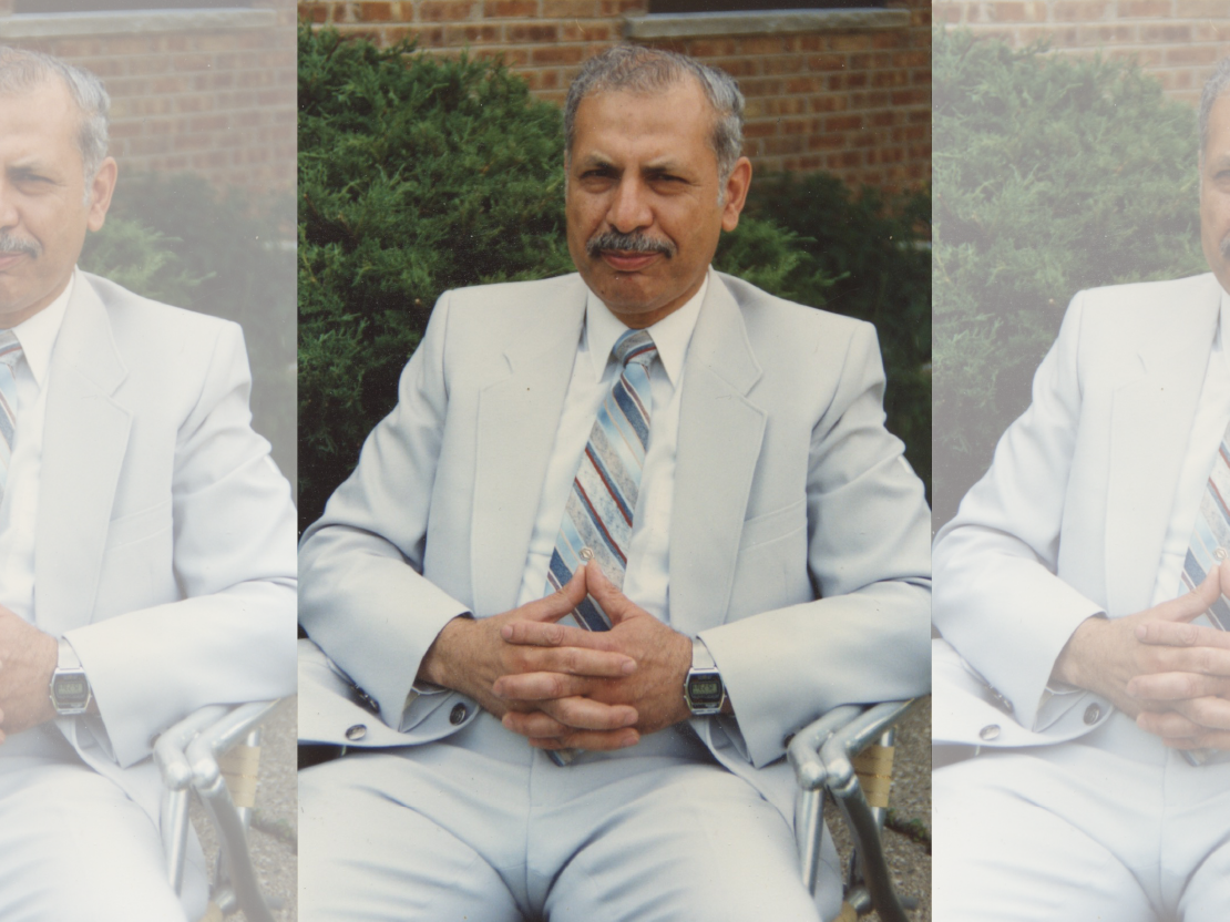 A color photograph showing an older Mahmoud Othman Atta wearing a light colored suit and tie, sitting in a chair, with his hands together on his lap.